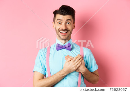 Valentines day and romance concept. Happy man in love holding hands on heart and looking with sympathy at lover, standing on romantic pink background 73628067