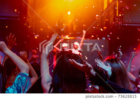 Group of people dance in disco night club to the beat of music from DJ on stage Group of people dance in disco night club to the beat of music from DJ on stage 73628815