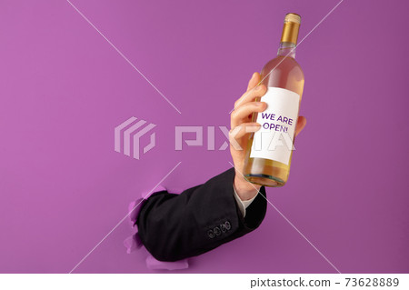 Male hand holding bottle of wine witrh label isolated on purple background. 73628889