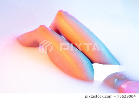 Close up female body in the milk bath with soft glowing in neon light Close up female body in the milk bath with soft glowing in neon light 73629004