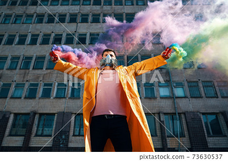 Young man in respirator mask hold smoke bombs in raised hands Young man in respirator mask hold smoke bombs in raised hands 73630537