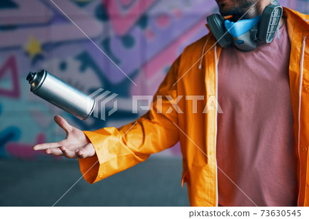 Graffiti artist throw his spray paint can against colorful graffiti Graffiti artist throw his spray paint can against colorful graffiti 73630545