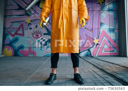 Cropped image of street artist with spray paint can in hand standing near the wall with his paintings Cropped image of street artist with spray paint can in hand standing near the wall with his paintings 73630563