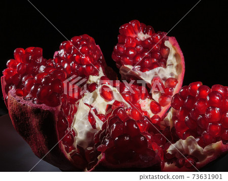 Pomegranate broken into pieces close-up on a black background. 73631901