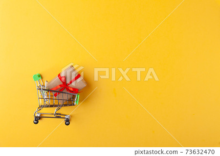 Gift box with red ribbon in mini grocery cart on pink background Gift box with red ribbon in mini grocery cart on pink background 73632470