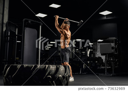Strong man hitting giant tire with sledgehammer. Strong man hitting giant tire with sledgehammer. 73632989