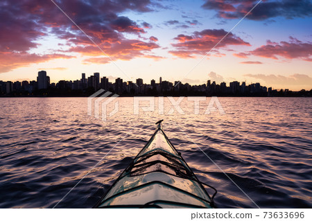 Sea Kayaking during a vibrant colorful sunrise with the city skyline in the background. 73633696