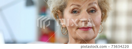 Slender elderly woman sits on sofa in an apartment 73634220