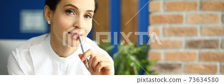 Employee holds a pen with her lips and thinks Employee holds a pen with her lips and thinks 73634580