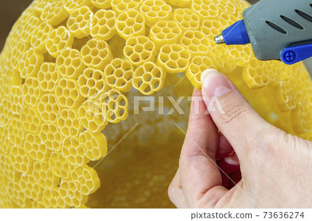 Woman glues pasta with a hot glue gun during the manufacture of crafts Woman glues pasta with a hot glue gun during the manufacture of crafts 73636274