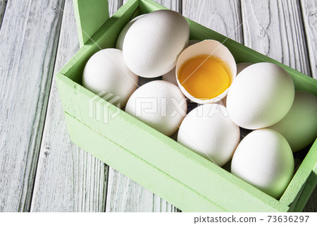 Close-up of fresh white organic chicken eggs and egg yolk in the green wooden box on light wooden background Close-up of fresh white organic chicken eggs and egg yolk in the green wooden box on light wooden background 73636297