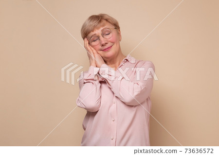 Mature woman sleeping tired dreaming and posing with hands together with closed eyes. 73636572