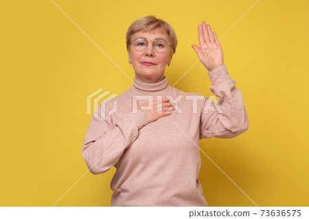 Serious patriotic woman raising one arm and putting on chest another making oath, swearing. 73636575