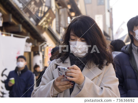 A woman wearing a mask operates a smartphone 73636692