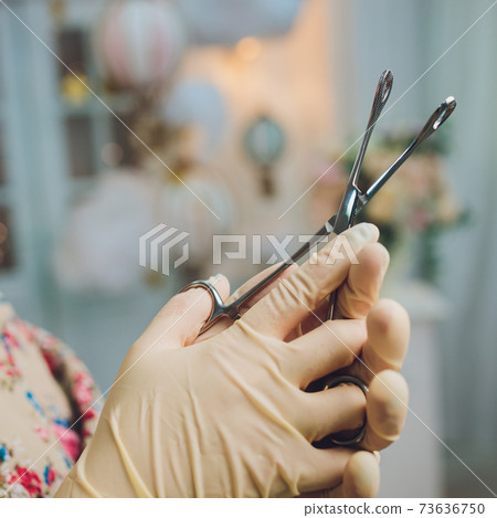 Doctor's hand in gloves and holding forceps. Doctor's hand in gloves and holding forceps. 73636750