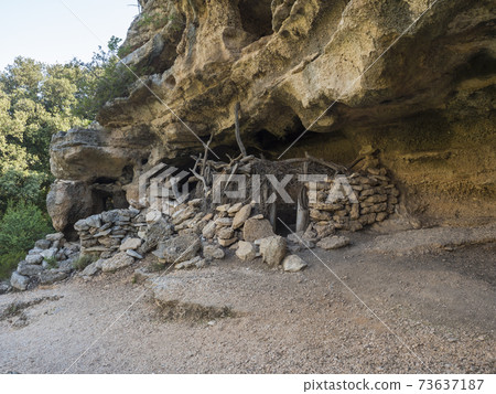 View of old cave shepard shelter on hiking path to Cala Goloritze beach with limestone rocks, trees, green bush. Gulf of Orosei, Sardinia, Italy, September View of old cave shepard shelter on hiking path to Cala Goloritze beach with limestone rocks, trees, green bush. Gulf of Orosei, Sardinia, Italy, September 73637187