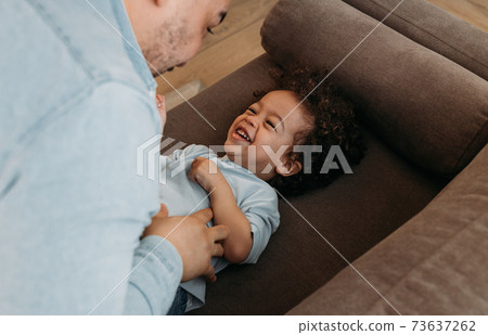 Close up of a father tickling laughing young boy on sofa 73637262