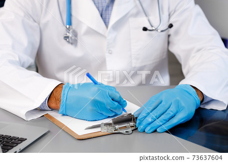 Hands of a doctor writing something on clipboard while sitting at working table Hands of a doctor writing something on clipboard while sitting at working table 73637604