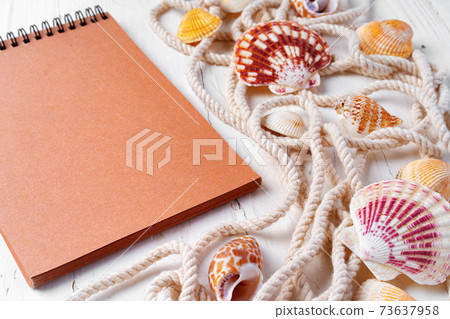 Close up photo of brown notepad with sea shells on wooden planks closeup Close up photo of brown notepad with sea shells on wooden planks closeup 73637958