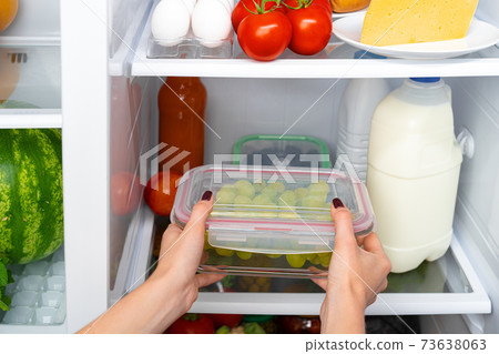 Female hands taking storage box with food from a fridge Female hands taking storage box with food from a fridge 73638063