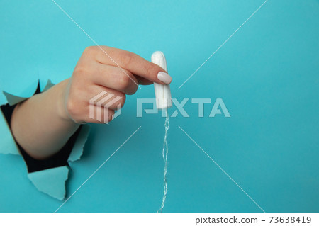 Female hand holds cotton tampon through torn paper background 73638419