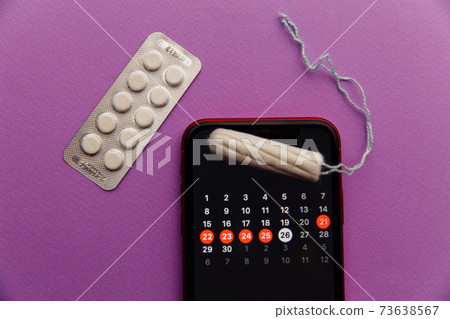 Menstruation app in smartphone with cotton tampon and red flower on a lilac background. Woman critical days and hygiene protection concept 73638567