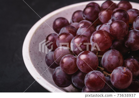 Fresh ripe grape berries in white wooden bowl on dark stone background, angle view macro Fresh ripe grape berries in white wooden bowl on dark stone background, angle view macro 73638937
