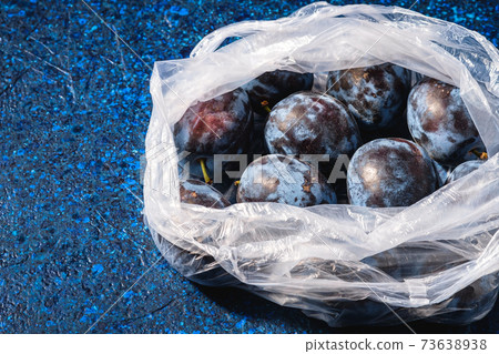 Fresh ripe plum fruits in plastic bag package on blue abstract background, angle view Fresh ripe plum fruits in plastic bag package on blue abstract background, angle view 73638938