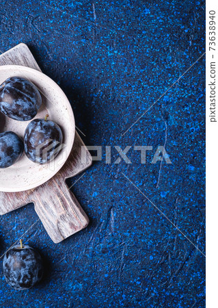 Fresh ripe plum fruits in white wooden bowl and old cutting board on blue abstract background, top view copy space Fresh ripe plum fruits in white wooden bowl and old cutting board on blue abstract background, top view copy space 73638940