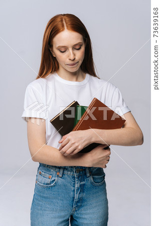 Beautiful sad young woman college student wearing T-shirt and denim pants holding book 73639168