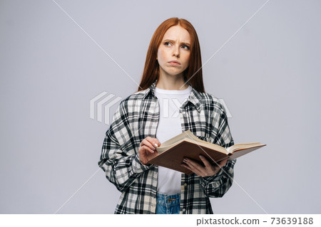 Thoughtful young woman college student turning pages of book on gray isolated background. Thoughtful young woman college student turning pages of book on gray isolated background. 73639188