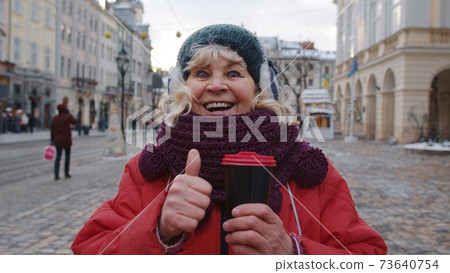 Senior woman grandmother tourist smiling, showing thumb up in winter city center of Lviv, Ukraine Senior woman grandmother tourist smiling, showing thumb up in winter city center of Lviv, Ukraine 73640754