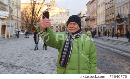 Senior man grandfather tourists traveling walking taking selfie pictures in European winter city Senior man grandfather tourists traveling walking taking selfie pictures in European winter city 73640776