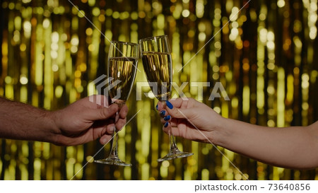 Two hands with glasses of champagne wine or cocktail making cheers, raising toast on gold background 73640856