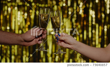 Two hands with glasses of champagne wine or cocktail making cheers, raising toast on gold background 73640857