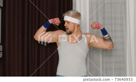Funny bodybuilder sportsman guy couch showing biceps, sport fitness boxing exercises with dumbbells Funny bodybuilder sportsman guy couch showing biceps, sport fitness boxing exercises with dumbbells 73640933