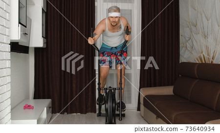 Funny athlete sportsman guy trainer on orbitrek recording sport fitness cardio online vlog at home Funny athlete sportsman guy trainer on orbitrek recording sport fitness cardio online vlog at home 73640934