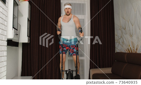 Sportsman retro guy in funny clothes making sport workout fitness cardio exercises on orbitrek home Sportsman retro guy in funny clothes making sport workout fitness cardio exercises on orbitrek home 73640935