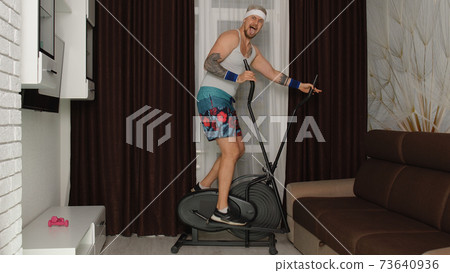 Funny man hipster athlete sportsman guy with beard makes workout fitness cardio on orbitrek at home Funny man hipster athlete sportsman guy with beard makes workout fitness cardio on orbitrek at home 73640936