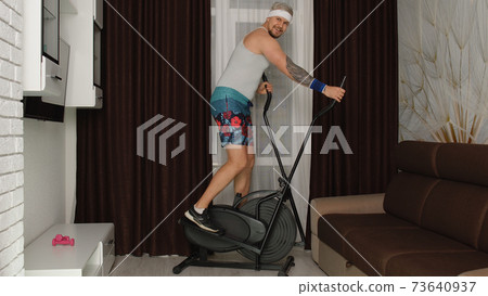 Funny athlete sportsman guy trainer on orbitrek recording sport fitness cardio online vlog at home 73640937
