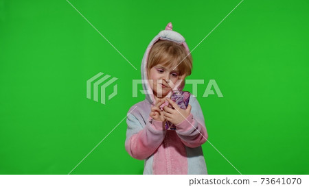 Excited little child girl in unicorn pajamas using mobile cell phone, found out great big win news 73641070