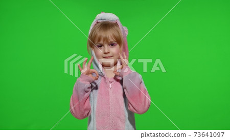 Little child girl smiling, showing ok gesture, agree sign in unicorn pajama on chroma key background 73641097