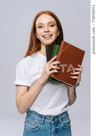 Cheerful young woman college student holding book and looking at camera on isolated background.  73649051
