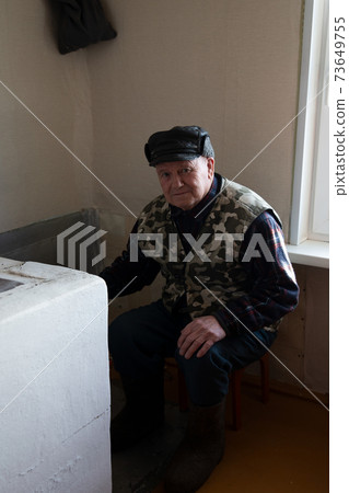 An old man puts wood in a heating stove in a country house in Russia, winter, Siberia An old man puts wood in a heating stove in a country house in Russia, winter, Siberia 73649755