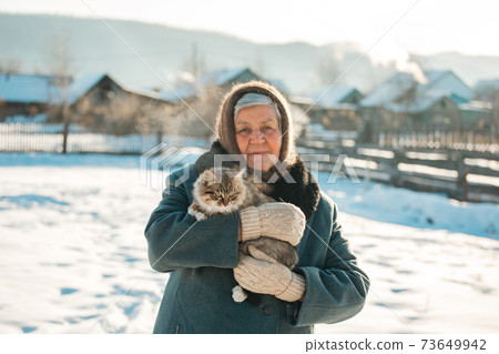 Russian grandmother holds a kitten in her arms, village, Siberia, winter Russian grandmother holds a kitten in her arms, village, Siberia, winter 73649942