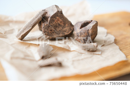 Chunks of roughly crushed chocolate or solid cocoa mass on craft paper. Chunks of roughly crushed chocolate or solid cocoa mass on craft paper. 73650448
