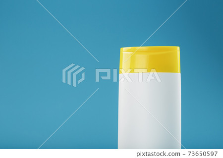 White plastic bottle with yellow cap with shampoo gel on blue background. White plastic bottle with yellow cap with shampoo gel on blue background. 73650597