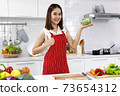 Happy Asian woman chef in red apron holding bowl of sunflower sprout in kitchen. 73654312