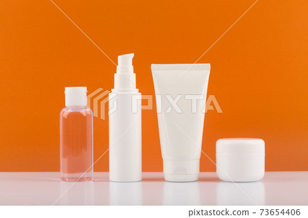 Set of skincare cosmetics on white glossy table against orange background. Concept of skincare and wellbeing Set of skincare cosmetics on white glossy table against orange background. Concept of skincare and wellbeing 73654406