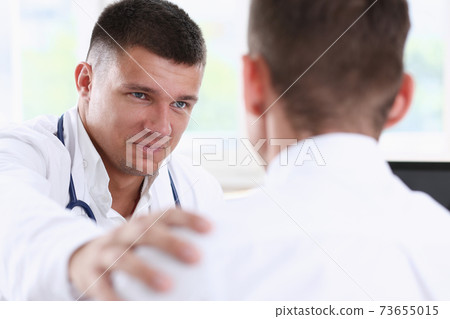 Friendly male doctor hold patient shoulder in office during reception Friendly male doctor hold patient shoulder in office during reception 73655015